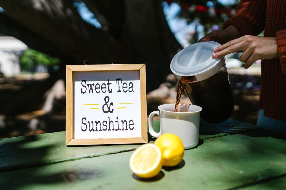 A glass pitcher of iced tea with lemon slices sits on a small wooden table.