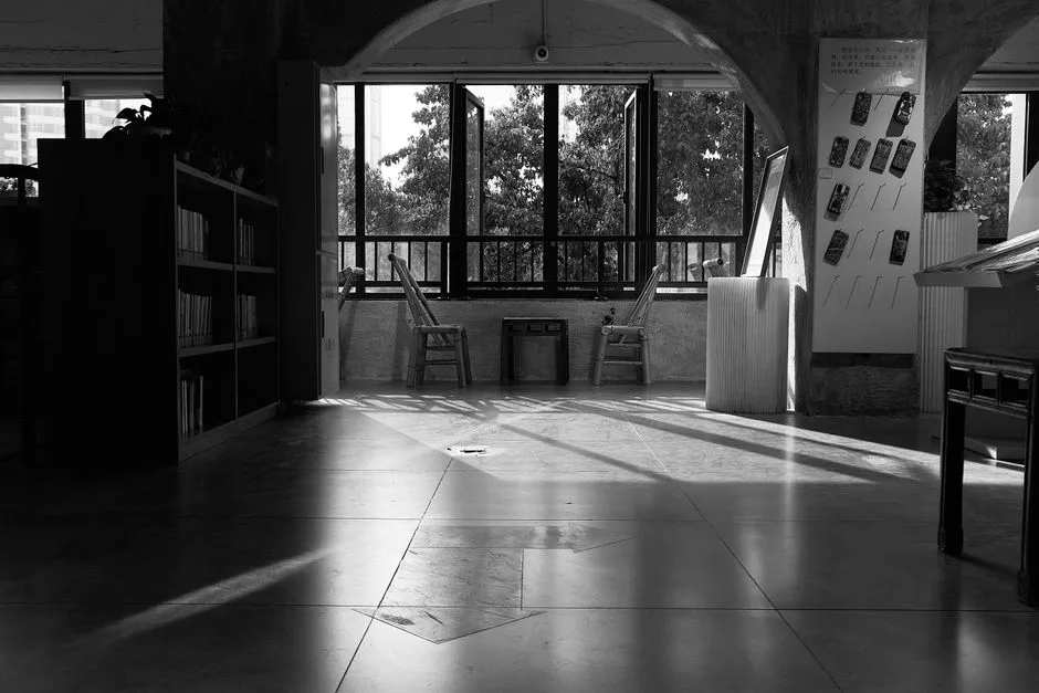 Sunlight streams through high arched windows onto wooden tables in a quiet library.
